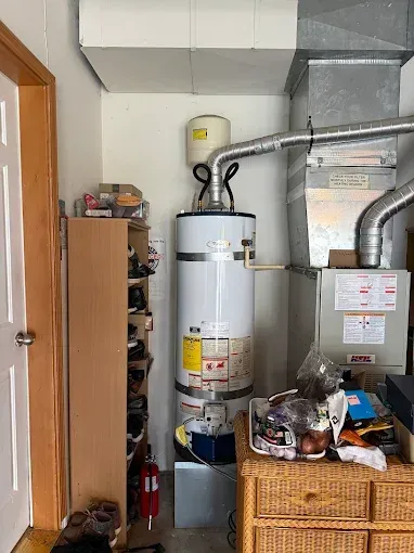 Utility room with a water heater, furnace ducts, and storage shelves beside woven baskets.