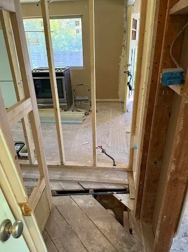 Partially demolished interior hallway with exposed framing, open doorway, and damaged floorboards