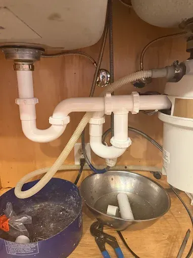 Under-sink plumbing with pipes, a bucket, and a sink basin in a cabinet space