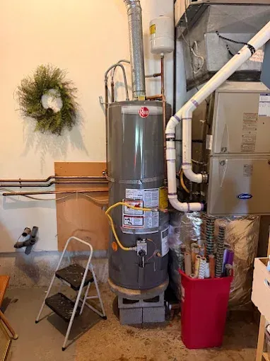 Water heater and furnace in a basement utility room with pipes, ducts, and a wreath on the wall