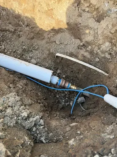 Broken blue cable and white pipe exposed in a dirt excavation site