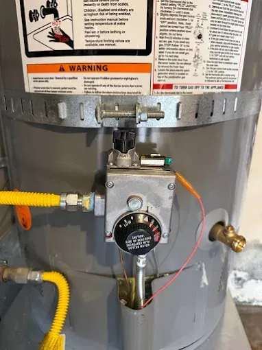Water heater gas control valve with yellow gas line and warning labels on gray tank.