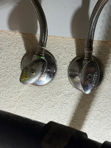 Two chrome shower heads mounted on a textured wall, one reflecting a fish-like face.