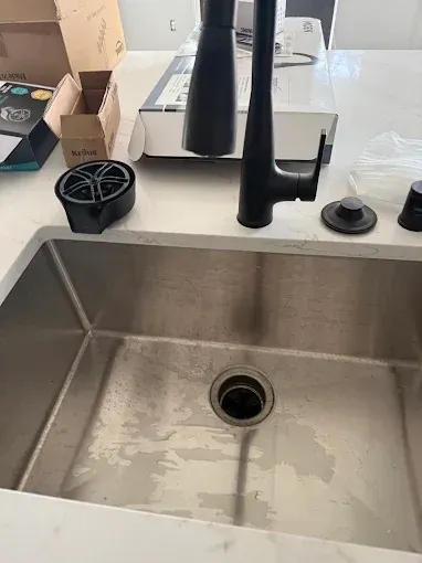 Stainless steel kitchen sink with black faucet and countertop items nearby, viewed from above