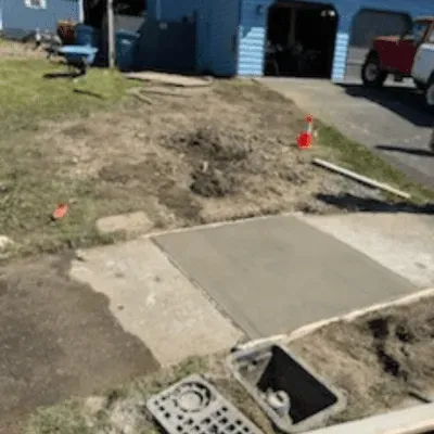 Damaged sidewalk with exposed utility opening beside a dirt trench and curb near parked vehicles
