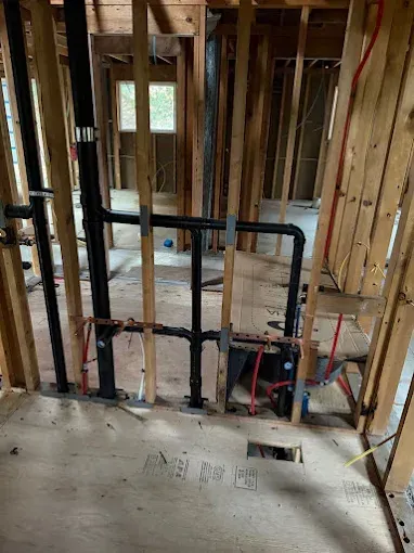 Unfinished interior wall framing with plumbing pipes and exposed studs in a remodel area.