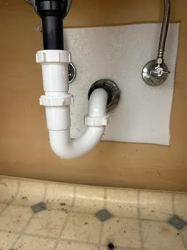 Under-sink drain pipe and P-trap installed through the cabinet wall on a tiled floor.
