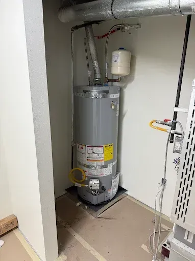 Utility closet with a water heater, exposed pipes, and a vented unit in a narrow alcove.