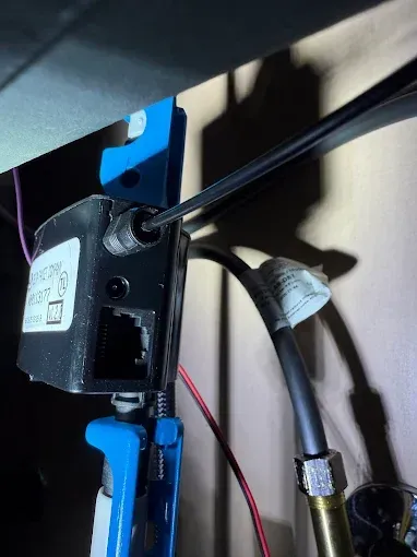Black cable connected to a small wall-mounted device with blue brackets and red wires nearby