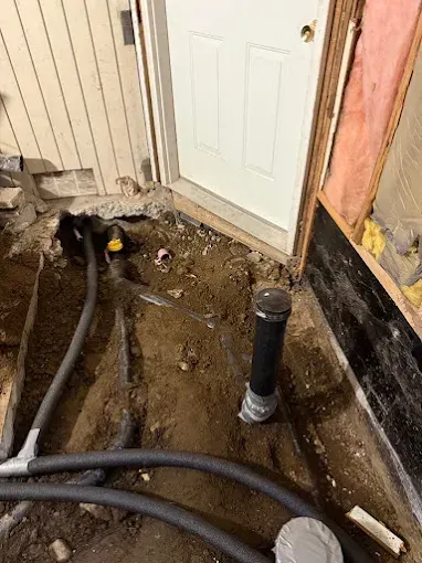Home renovation worksite with exposed dirt floor, black pipes, and a white door beside damaged wall framing