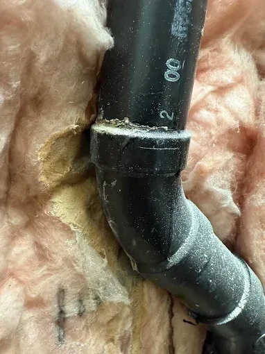 Black cable against tan insulation, showing a taped connection on a wall or ceiling.