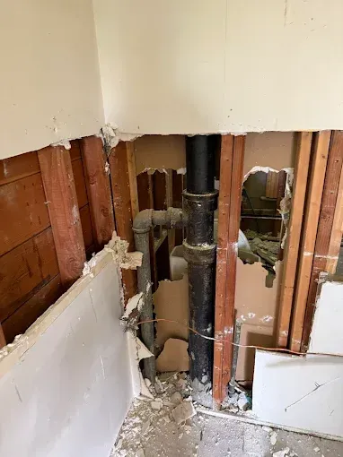 Damaged wall exposing plumbing pipes and torn drywall in a renovation area