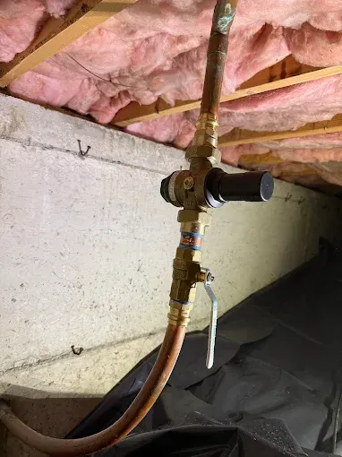 Plumbing valve and copper pipe beneath pink insulation in a basement crawlspace