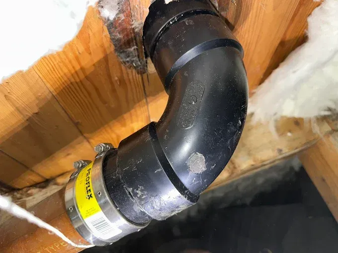 Black PVC pipe elbow joint beneath wood framing with white insulation nearby