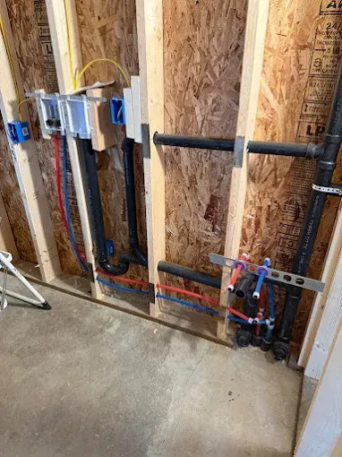 Plumbing and electrical rough-in inside unfinished wall framing in a construction site