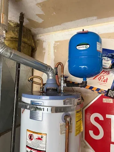 Water heater with blue expansion tank and metal vent pipes in a utility closet