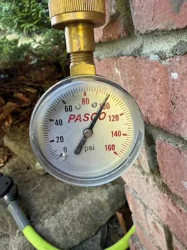 Pressure gauge mounted on a brick wall, showing PSI readings in red and black.