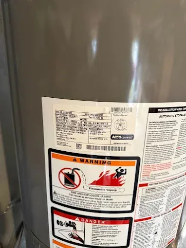 Close-up of a water heater with warning labels and instructions on the front.