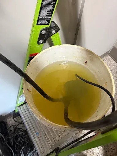 White bucket of yellow liquid with two black hoses on a green cart in a work area