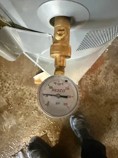 Pressure gauge attached to the bottom of a water heater, reading low pressure