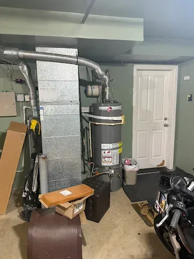 Basement utility area with water heater, HVAC ductwork, and a white door beside stored items.