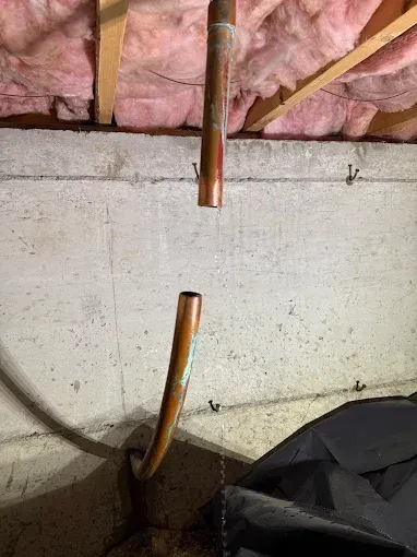 Basement wall with copper pipes and pink insulation above a concrete ledge