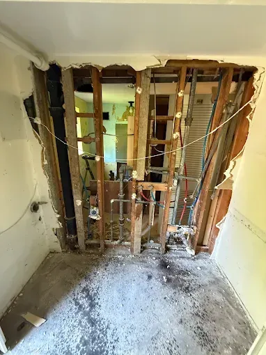 Partially demolished room with exposed wall studs, debris on the floor, and damaged drywall and wiring.