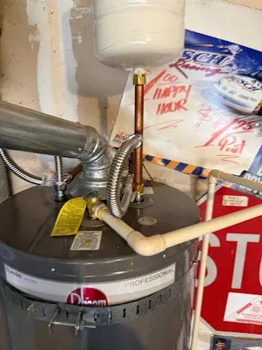 Water heater with pipes and venting in a utility closet, with insulation and store signs in the background