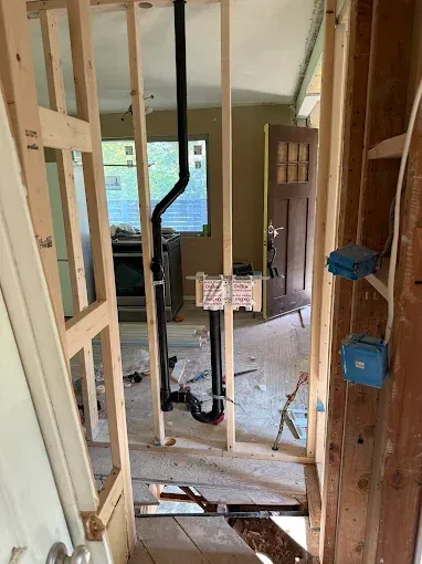 Interior under renovation with exposed wall studs, door frame, and unfinished flooring.