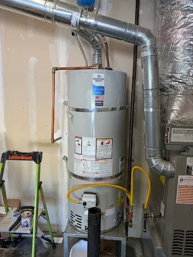 Water heater in a utility room with silver ductwork and a yellow hose attached.