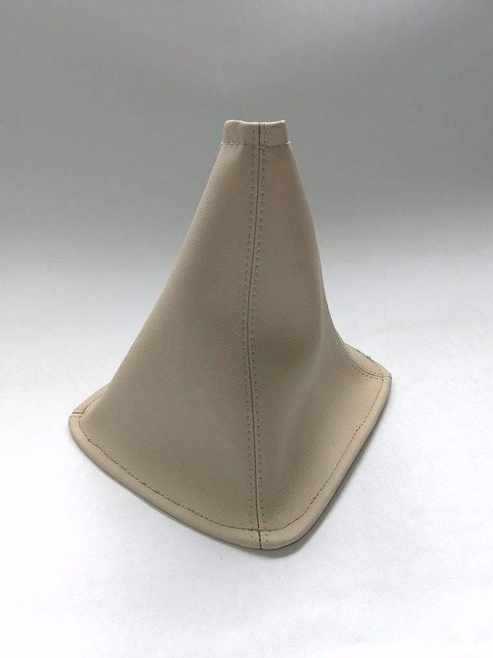 Funda de palanca de cambios de cuero beige para coche con costuras cosidas sobre fondo blanco.