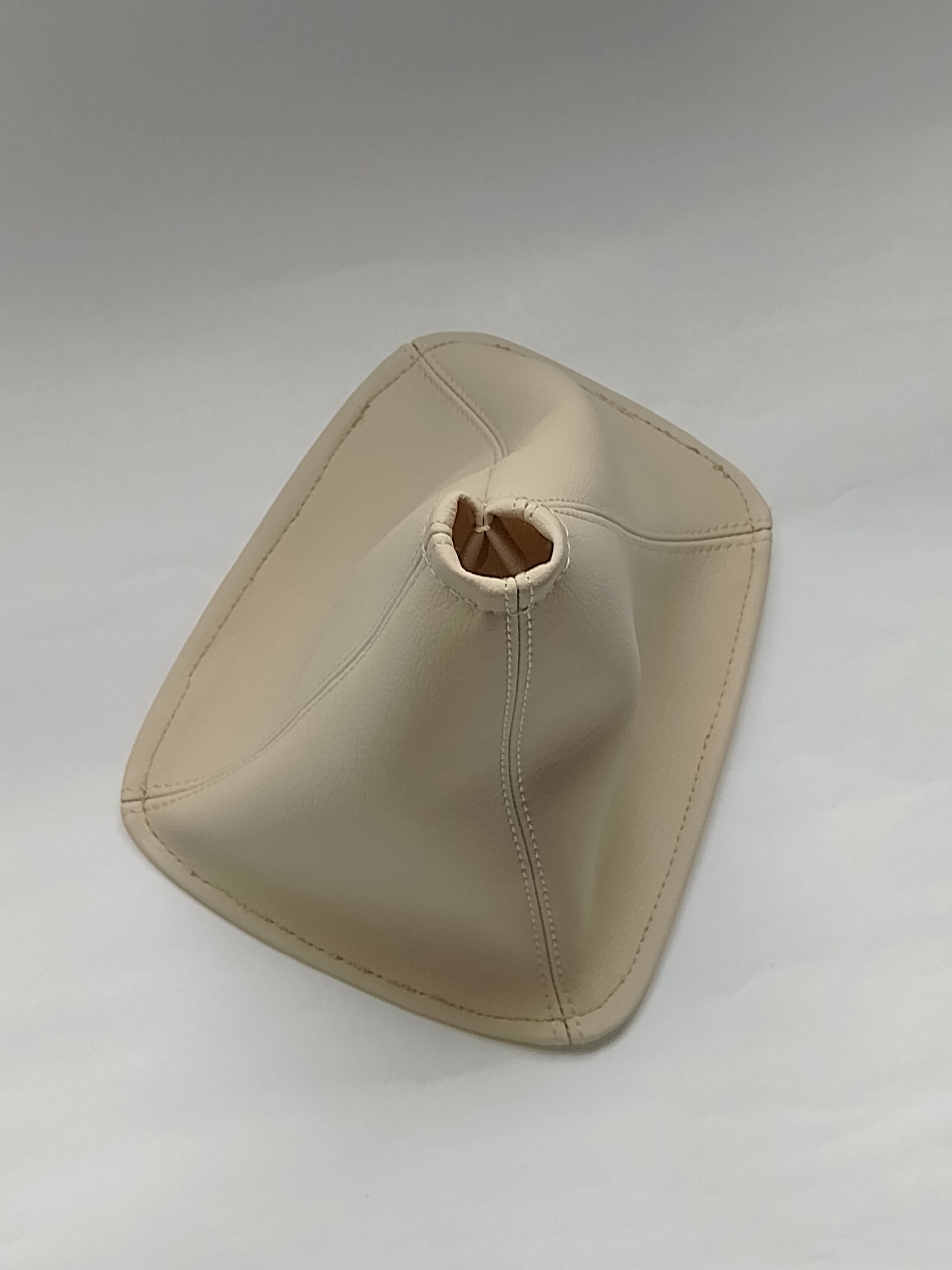 Funda de palanca de cambios de cuero beige para coche con costuras cosidas sobre fondo blanco.