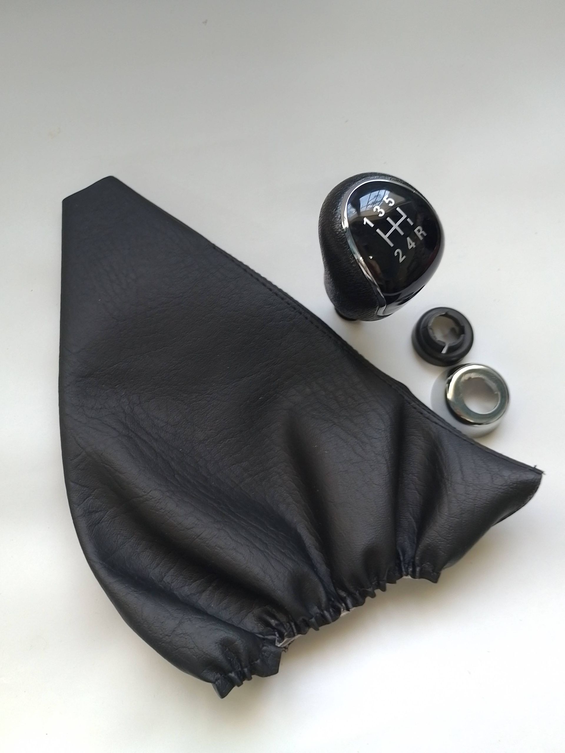 Funda de palanca de cambios de cuero negro con dos anillos cromados y pomo de palanca de cambios negro sobre fondo blanco.