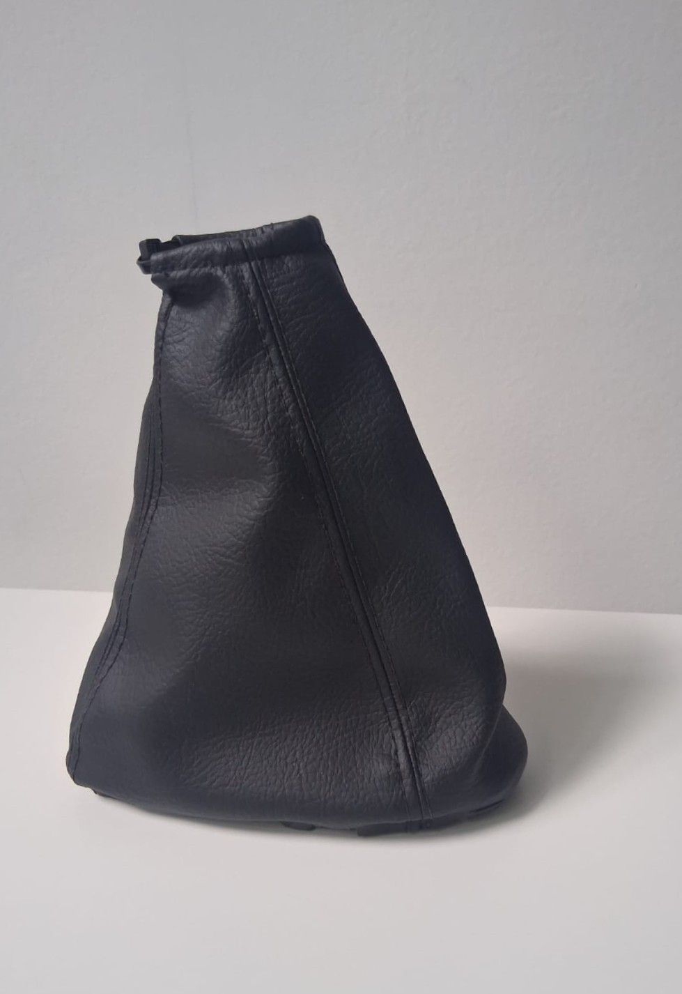 Bolsa de cuero negro con cordón ajustable, colocada en posición vertical sobre una superficie blanca.