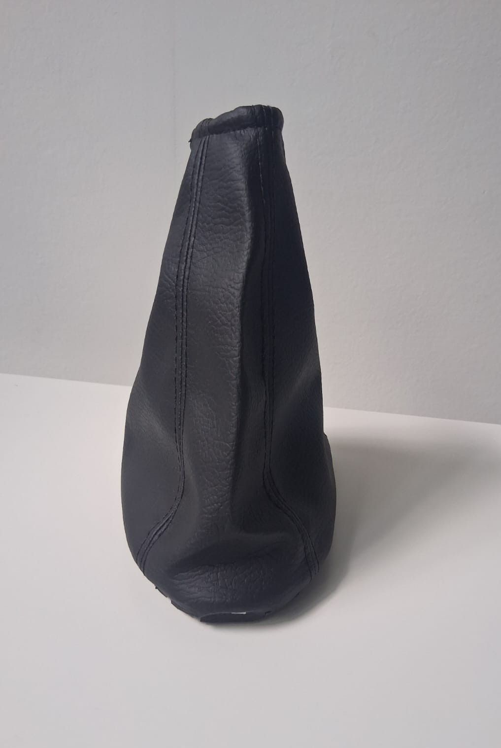 Bolsa de cuero negro con cordón ajustable, colocada en posición vertical sobre una superficie blanca.