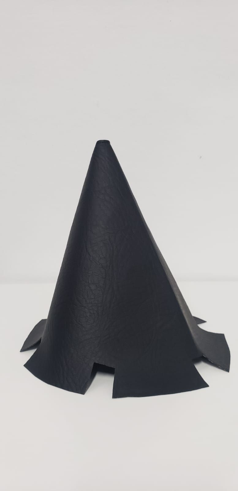 Objeto negro en forma de cono con una base recortada sobre un fondo claro liso.