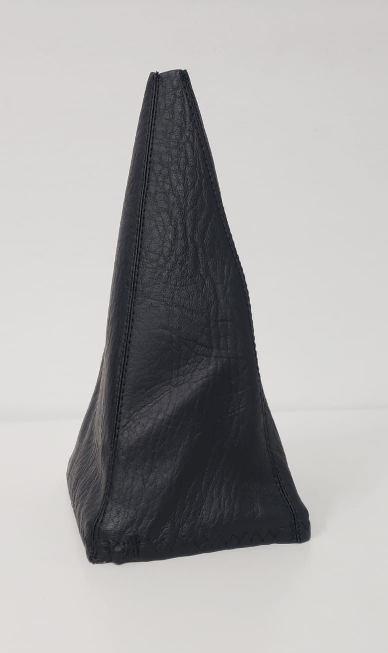Puf o taburete triangular de cuero negro sobre un fondo claro liso.