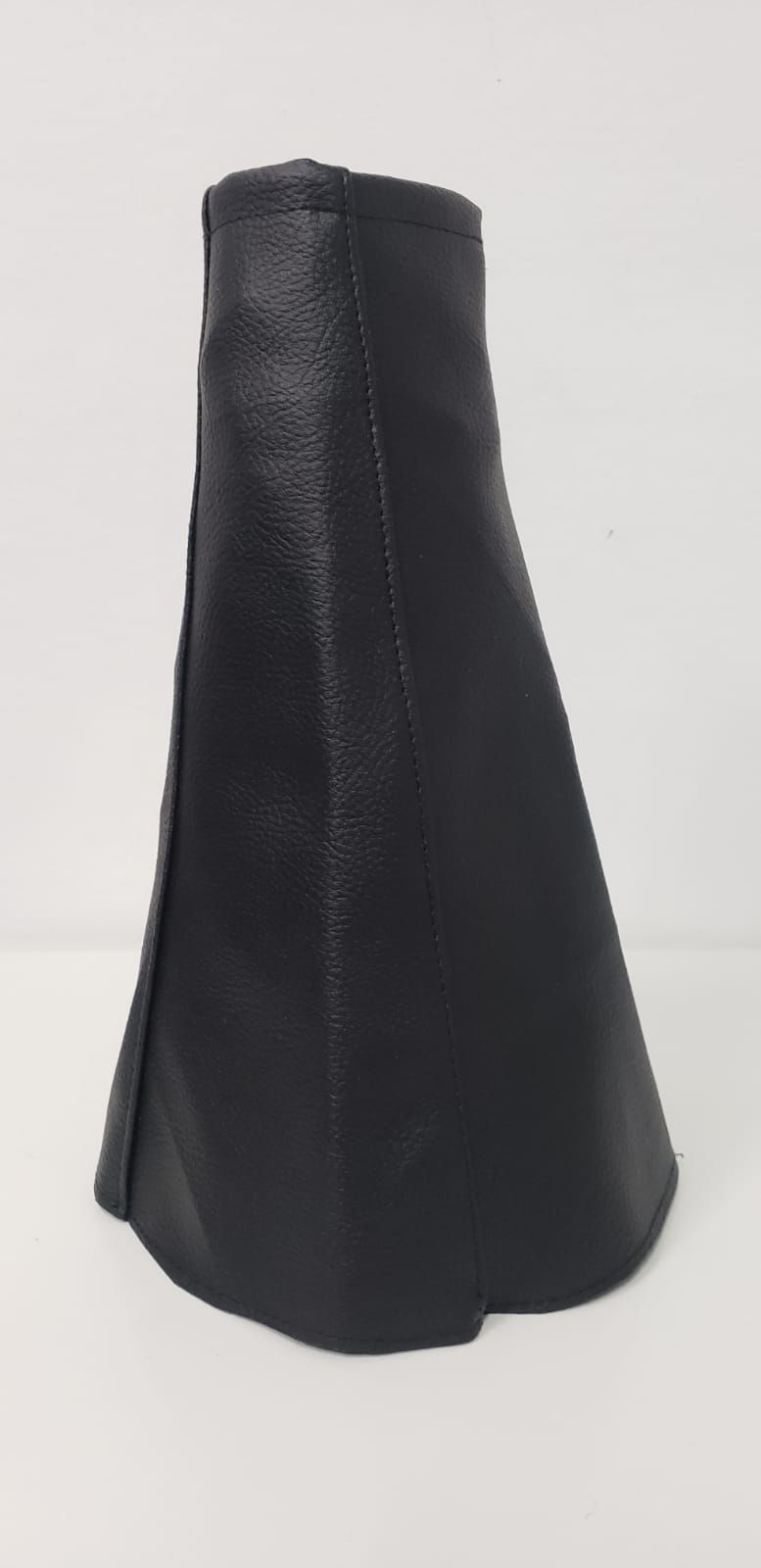 Objeto de cuero negro en forma de cono sobre un fondo blanco liso.