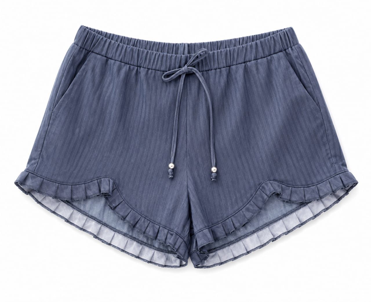 Persona con camiseta estampada de color beige y pantalones cortos azules de pie al aire libre en un sendero polvoriento, con las manos en los bolsillos.