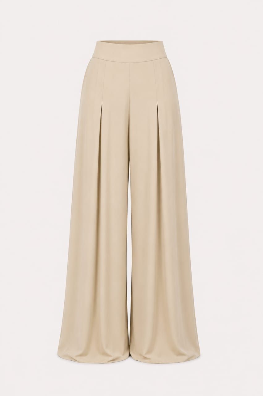Mujer con top blanco sin tirantes y pantalones anchos de color beige de pie en una terraza junto al agua.