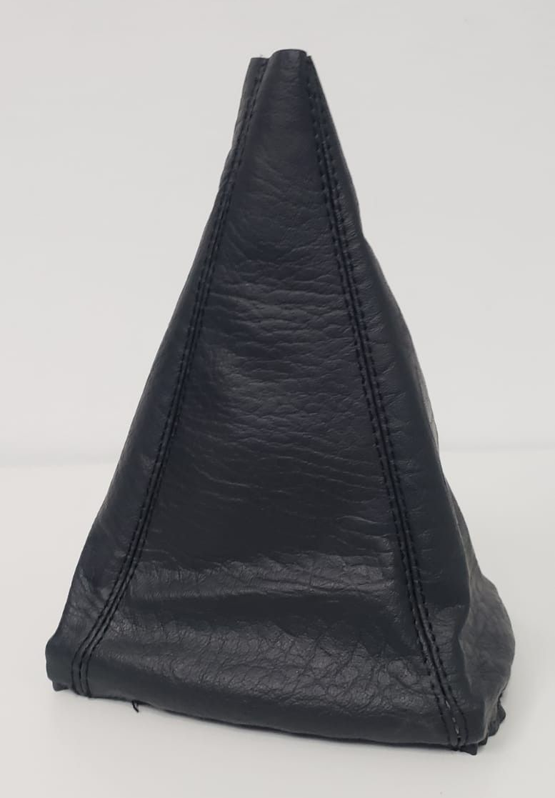 Puf o taburete triangular de cuero negro sobre un fondo claro liso.