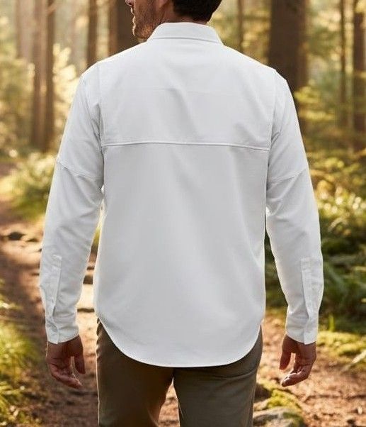 Hombre con camisa blanca y pantalones color canela, con mochila, de pie al aire libre al atardecer, con vistas a las montañas.