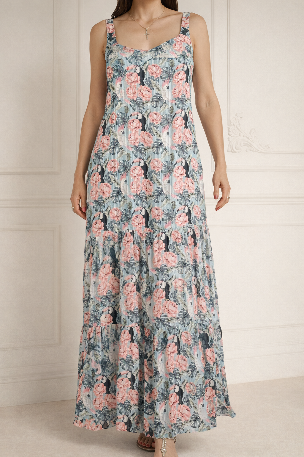 Mujer con vestido largo sin mangas de estampado floral rosa y verde contra una pared clara
