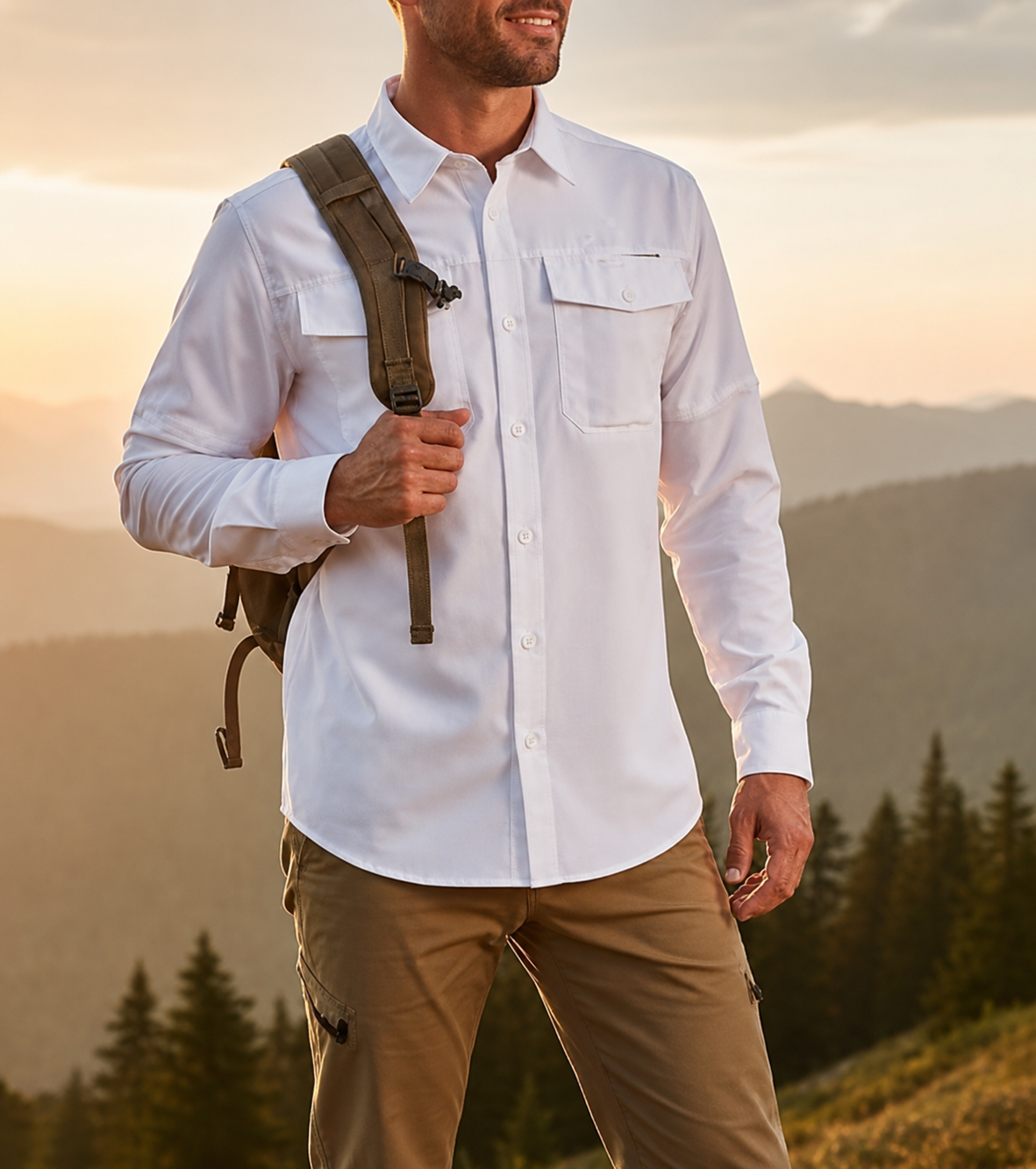 Hombre con camisa blanca y pantalones color canela, con mochila, de pie al aire libre al atardecer, con vistas a las montañas.