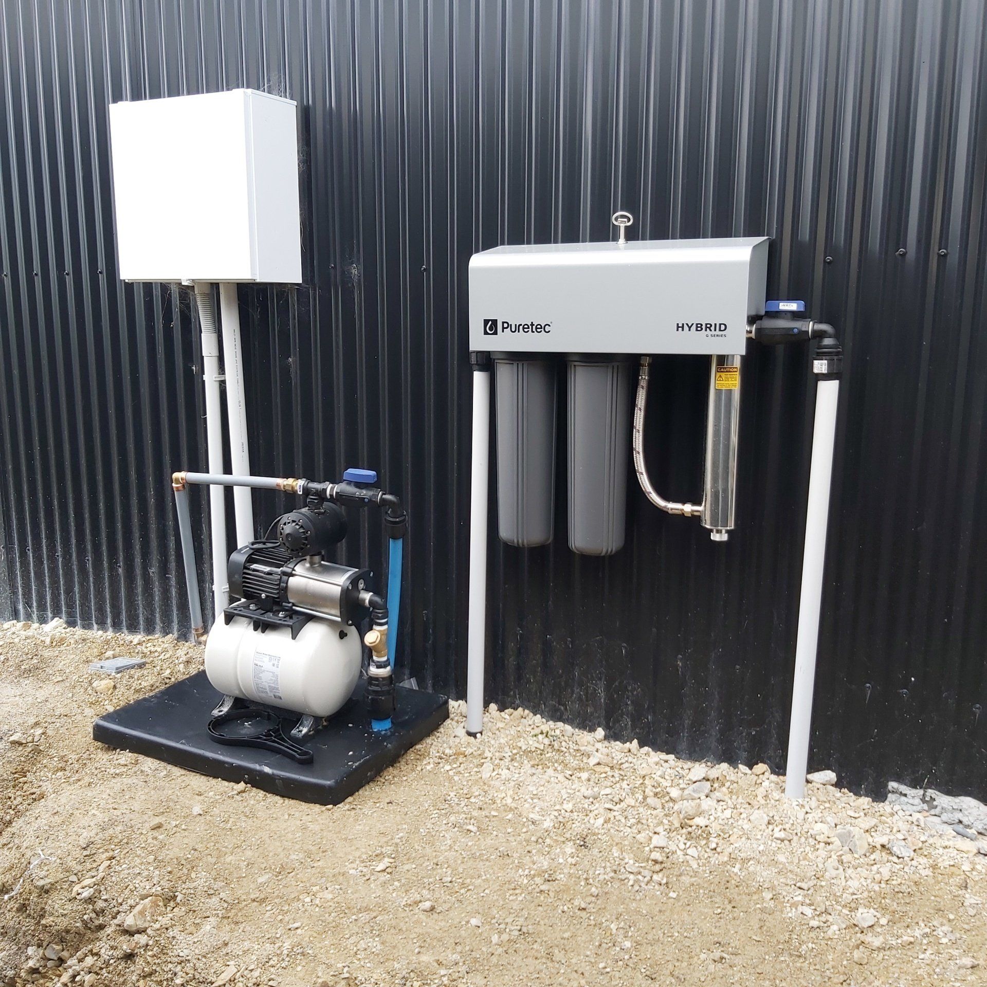 A water pump and filtration system installed against a corrugated black wall.