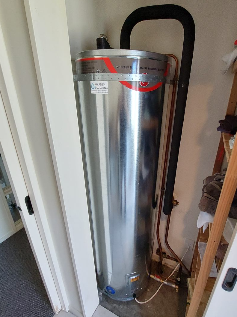 A tall, silver water heater is in a corner, with black insulated pipe and copper pipes.