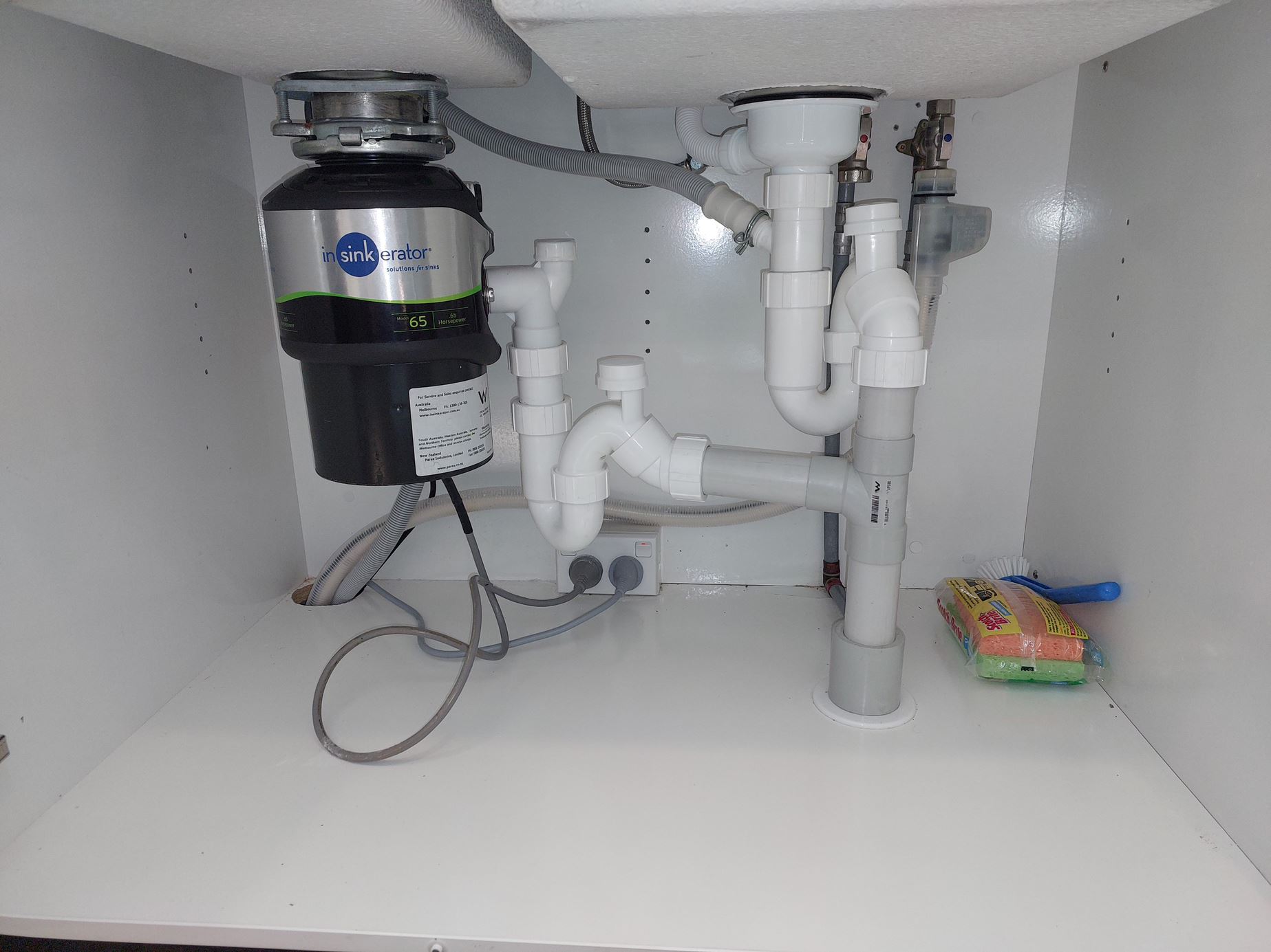 Under-sink plumbing with a garbage disposal unit, featuring white pipes, a black disposa.