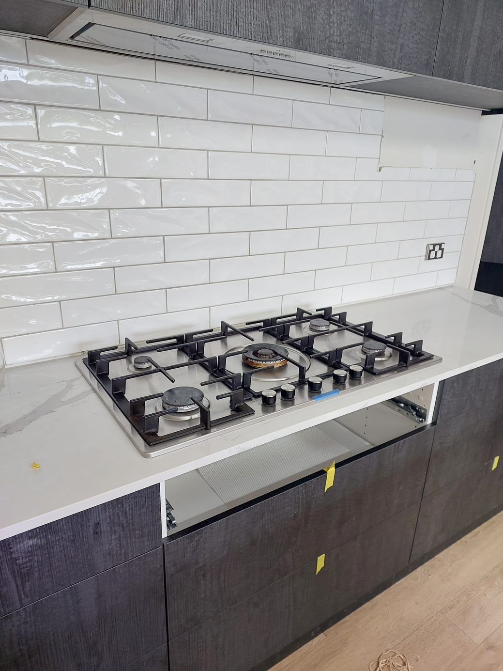 Kitchen with a gas cooktop and white subway tile backsplash, dark cabinets, and a white countertop.