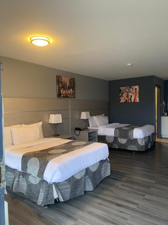 Hotel room with two queen beds, lamps, gray walls, and artwork. Wooden floor.