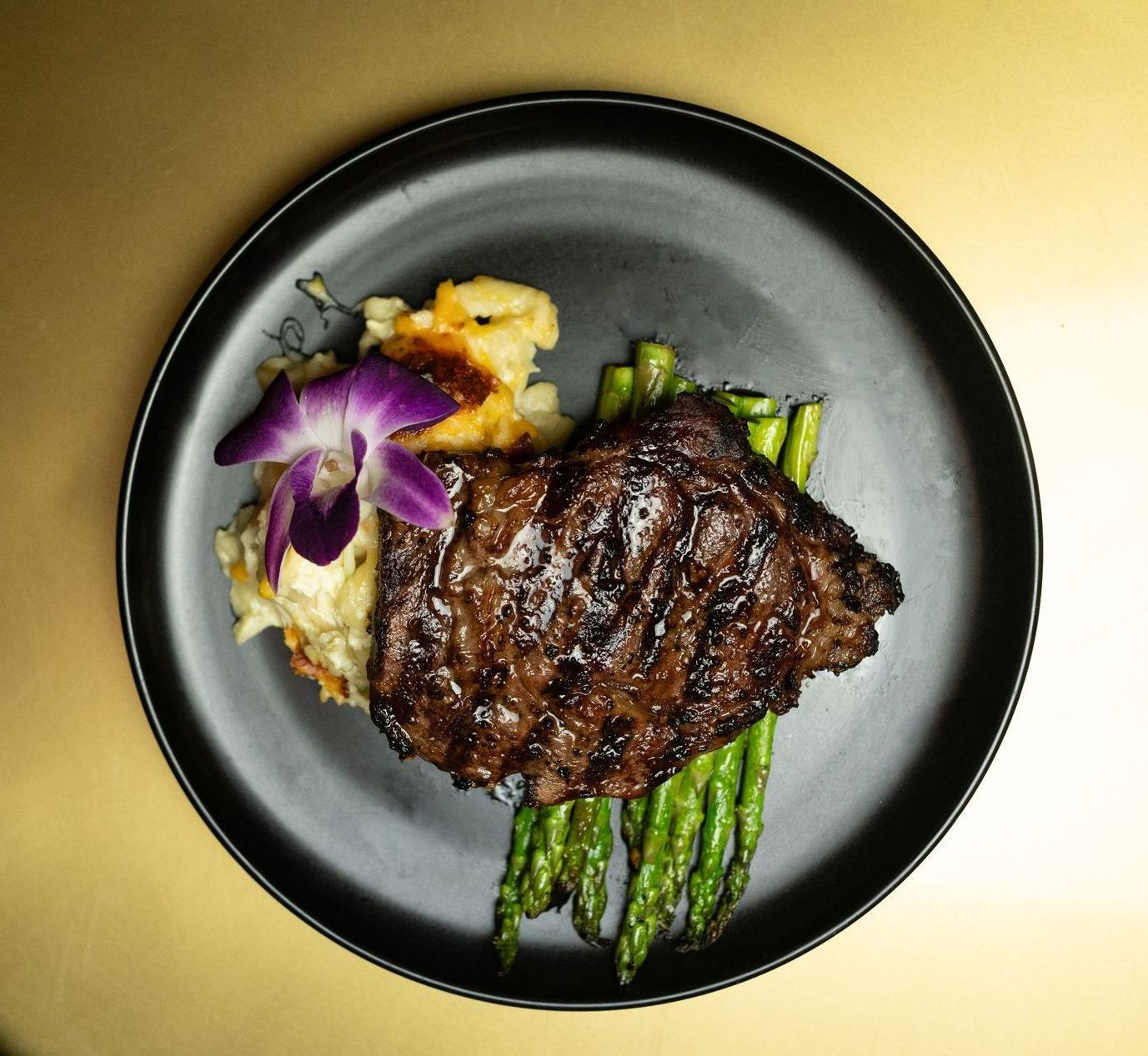 A steak with asparagus and mashed potatoes on a black plate